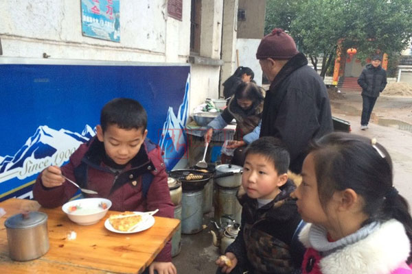 Students of Huangtankou Primary School eat breakfast at Huang Shihua's food stall. [Photo/Zhejiang News]