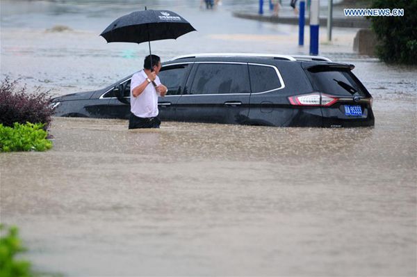 A man walks past a stranded vehicle on a flooded road in Jiujiang City, east China's Jiangxi Province, July 2, 2016. Heavy rainstorm hit the city on Saturday. [Photo/Xinhua]