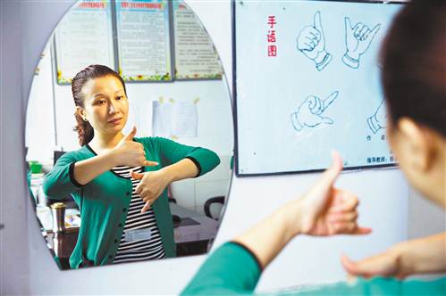 Zhou Juan practices sign language in front of a mirror.