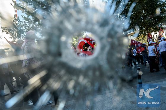 Demonstrators seen through a hole in hotel's a window near Istanbul's Taksim Square wave Turkish flags on July 24, 2016 during the first cross-party rally to condemn the coup attempt against President Recep Tayyip Erdogan. [Photo/Xinhua]