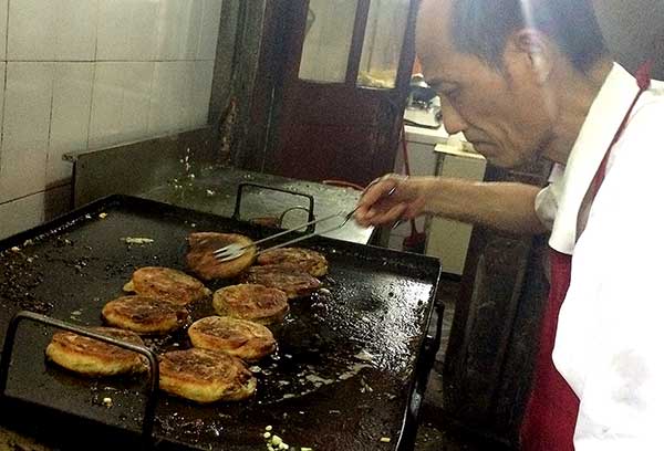 Wu Gencheng prepares spring onion pancakes in his stall in Shanghai on Monday.[Yin Liqin/for China Daily] 