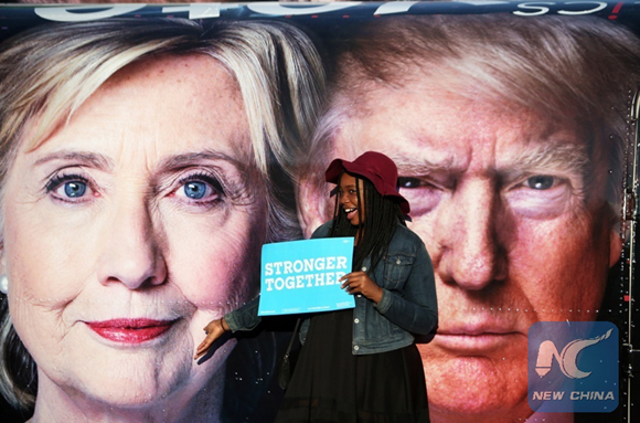 A girl poses for photos with Hillary Clinton and Donald Trump posters at Hofstra University in New York, the United States on Sept. 26, 2016. [Photo/Xinhua]