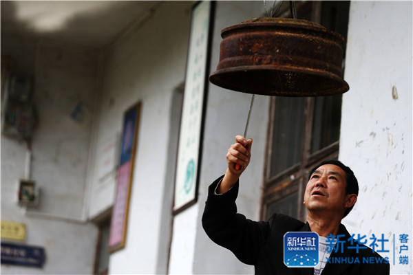 Yang Jinhua, the only teacher in Muqiao primary school, hits the clock made from a car tire on October 24, 2016. [Photo: Xinhua]