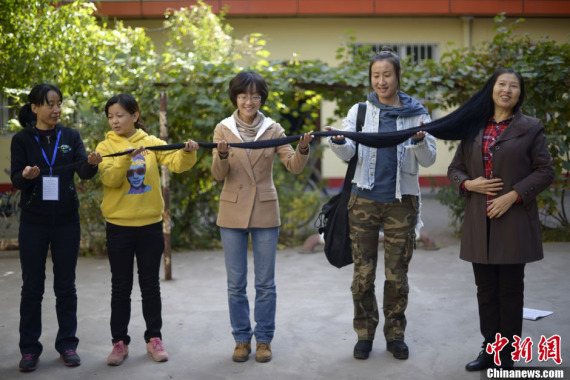 File photo of Ni Linmei (R) demonstrating her hair, which was then 2.9 meters in length, with the help of her friends in October,2013.(Photo: China News Service)