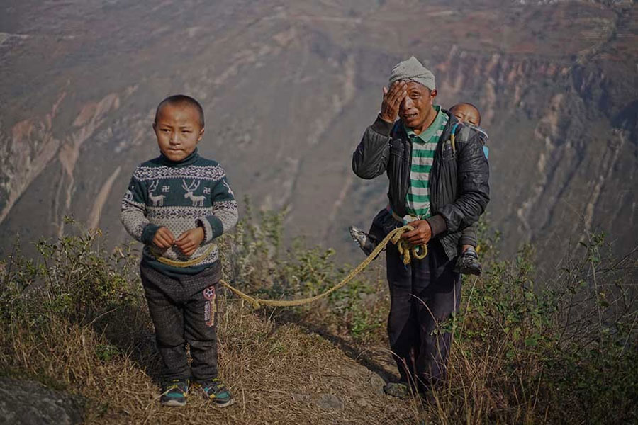A villager, carrying his 4-year-old son on his back, drags another 7-year-old son with a rope to ensure he is safe as he climbs the steel ladders to the cliff village in Sichuan province on Saturday, November 19, 2016. [Photo: The Beijing News]