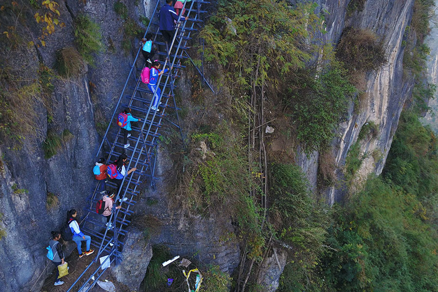 Children climb a steel ladder to the cliff village in Sichuan province on Saturday, November 19, 2016. The old rattan ladders nearby remain but are no longer used. [Photo: The Beijing News] 