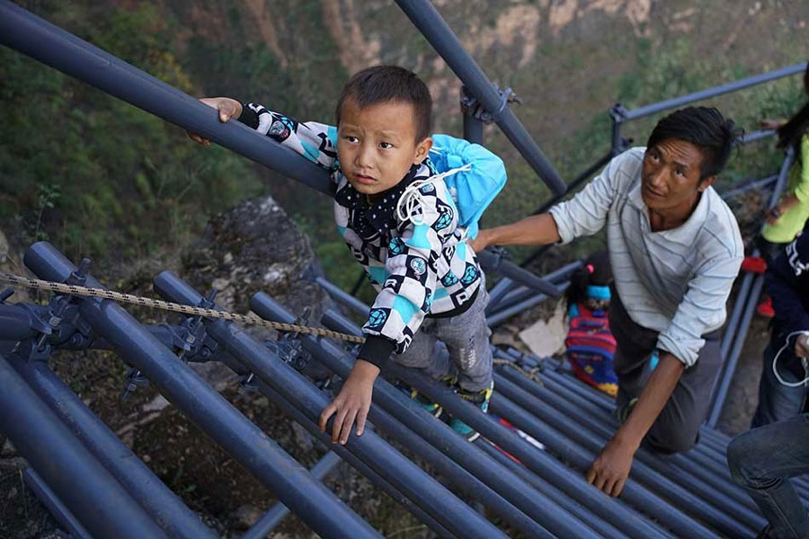 A father protects his son from behind as they climb the steel ladders to the cliff village in Sichuan province on Saturday, November 19, 2016. [Photo: The Beijing News] 