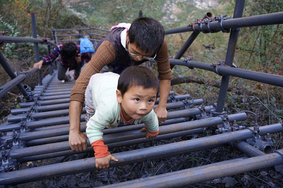 A father protects his son from behind as they climb the steel ladders to the cliff village in Sichuan province on Saturday, November 19, 2016. [Photo: The Beijing News] 