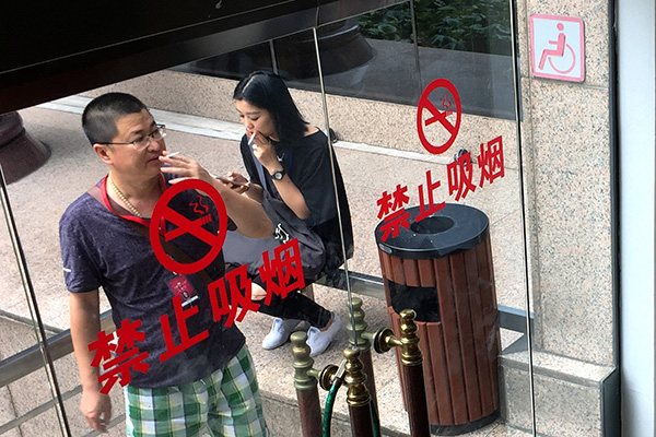 People smoke at an outdoor designated smoking area on Dongfang Road in Shanghai in September. The city will extend its public smoking ban to more outdoor areas under a new regulation starting in March. [Photo/China Daily]