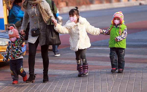 A woman and three children make their way through heavy smog in Dongzhimen, Beijing, on Sunday. [Photo by Zou Hong/China Daily]