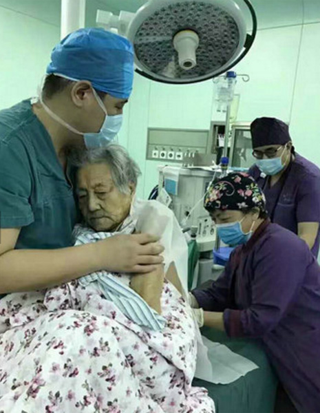 Doctor Zhao Liang holds the 102-year-old woman patient in his arms and comforts her as she is given anesthesia. [Photo/WeChat]