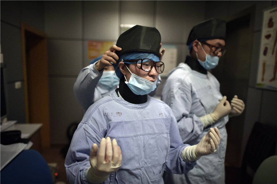 A medical staff adjusts a lead-made hat before she goes into the surgery room for an operation. [Photo by Ran Wen/for China Daily] 