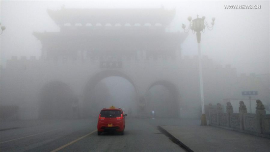 A car runs in the fog-bound county seat of Runan, central China's Henan Province, Jan. 3, 2017. A red alert for fog in large parts of China was issued by the National Meteorological Center on Tuesday. [Photo/Xinhua]