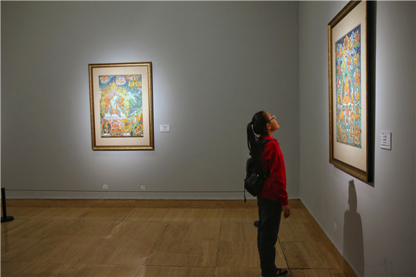 A girl visits the ongoing thangka exhibition, Heavenly Tibet, at Beijing's National Art Museum of China. The dozens of paintings on show mostly feature Buddhist thangka produced in recent years. [Photo by Jiang Dong/China Daily]