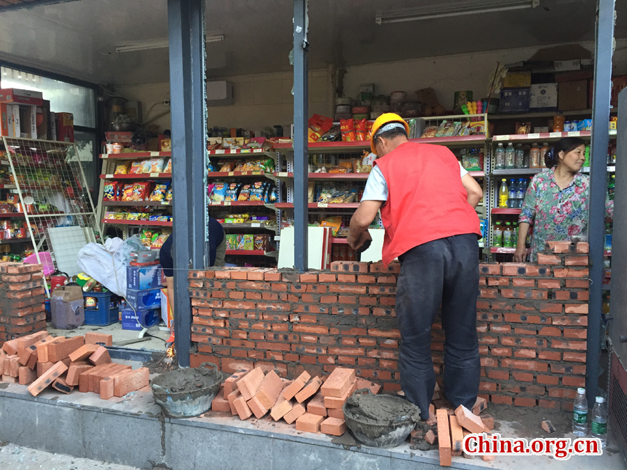 A shopkeeper watches on as her shop is bricked up on South Jianzi Alley, Beijing, on May 23, 2017. [Photo by Christopher Georgiou / China.org.cn] 