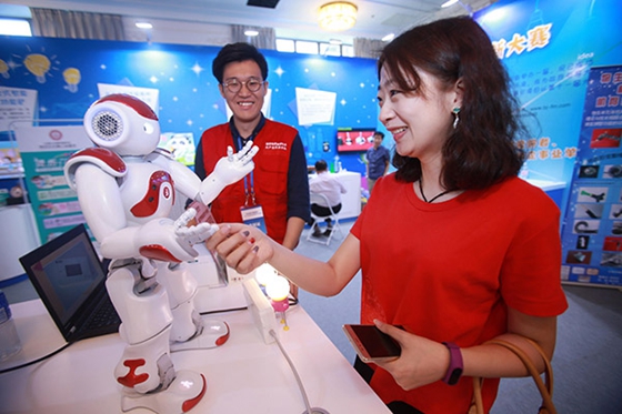 A visitor shakes hands with a robot during a science and technology week in Beijing. [Photo/China Daily]