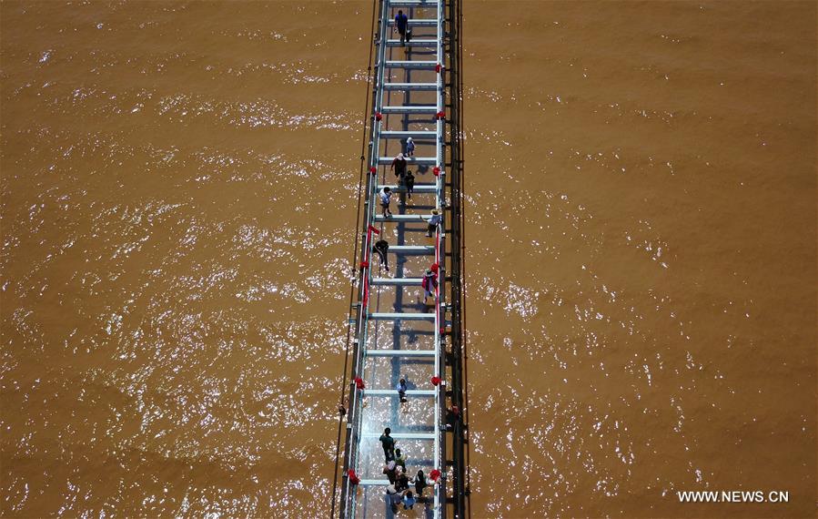 Tourists walk on a glass bridge across the Yellow River in Zhongwei, northwest China&apos;s Ningxia Hui Autonomous Region, Aug. 2, 2017. The 210-meter-long glass bridge was modified from an old suspension bridge by replacing the wooden deck with glass. (Xinhua/Li Ran)