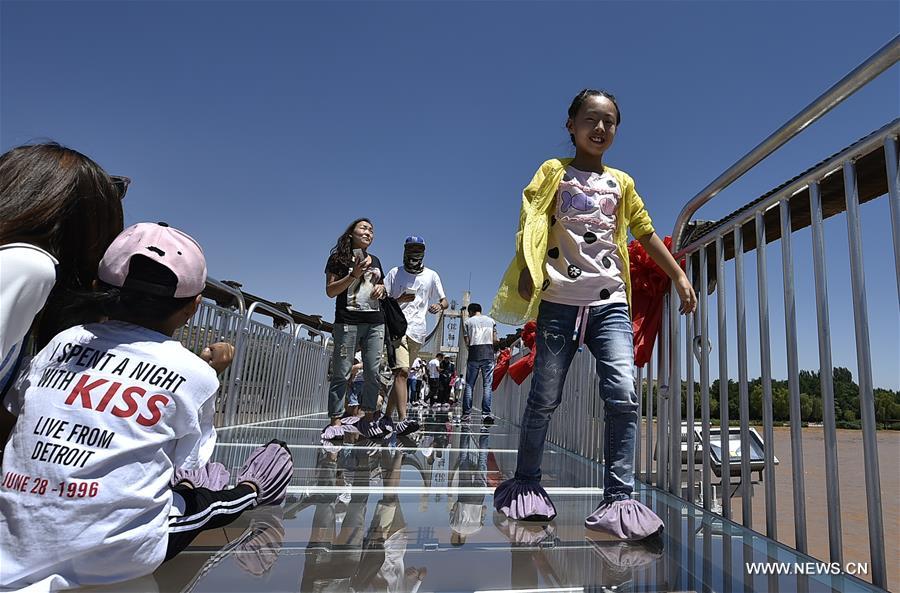 Tourists walk on a glass bridge across the Yellow River in Zhongwei, northwest China&apos;s Ningxia Hui Autonomous Region, Aug. 2, 2017. The 210-meter-long glass bridge was modified from an old suspension bridge by replacing the wooden deck with glass. (Xinhua/Li Ran)