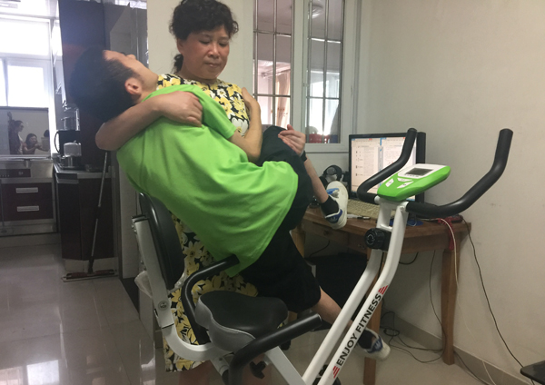 Guan Ping lifts Liguan onto an exercise machine in their home. [Photo by Tan Yingzi/China Daily]