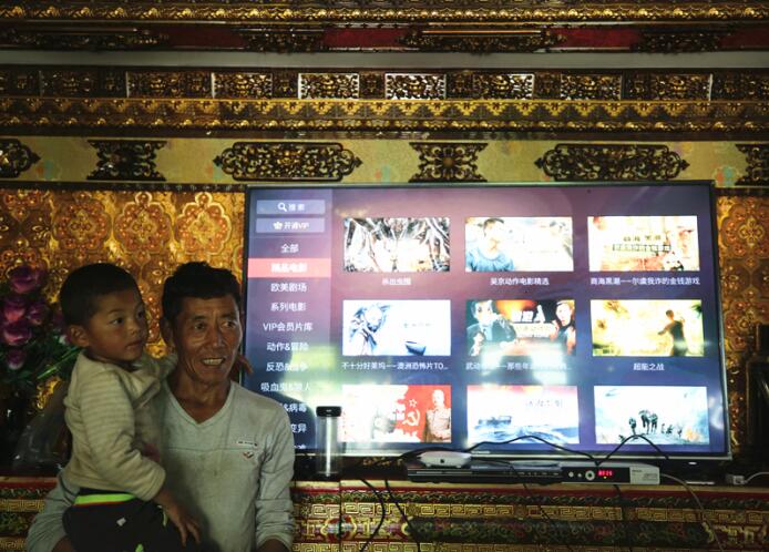Ciren Gesang, a resident in Zhaxi Tuomen community of Shannan Prefecture, China’s Tibet Autonomous Region, stands in front of the internet television with his son in his hands. [Photo by Zhang Jiaqi / China.org.cn]