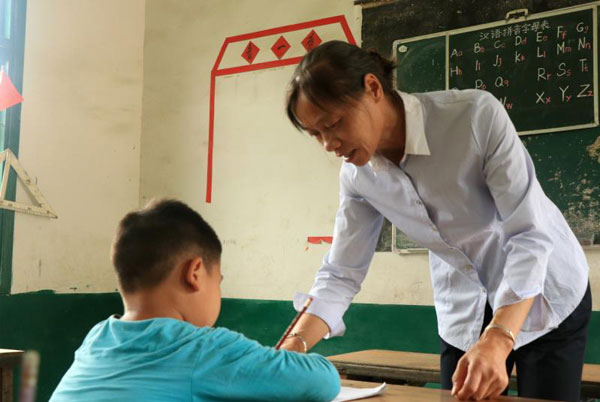 Yu Xiaoli helps a student with his studies in a class in Zongshujiao village in Central China's Hunan province.[Photo by Hu Jiangyong / chindaily.com.cn]