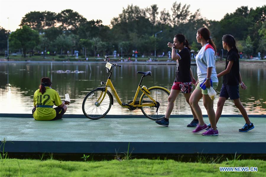People walk past an ofo sharing-bike at a public park in Phuket, Thailand, Oct. 5, 2017. China's dock-less bike-sharing company ofo provided more than 1,000 bikes in Phuket's key locations in late September and offered a 1-month free trial without deposit fee. Now the bike-sharing service has benefited local residents and tourists. Ofo's regular service fee will be charged at 5 Baht per 30 minutes usage, with a deposit fee of 99 Baht. [Photo/Xinhua]