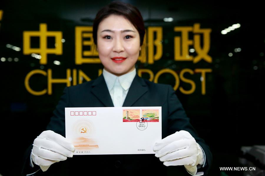 A postal staff member shows a first day cover in Shijiazhuang, north China&apos;s Hebei Province, Oct. 18, 2017. China Post issued a set of commemorative stamps marking the 19th National Congress of the Communist Party of China on Wednesday. The set consists of two stamps and a stamp sheetlet. (Xinhua/Zhan Xincheng)