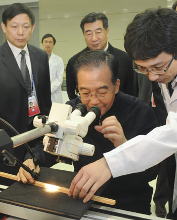 Chinese Premier Wen Jiabao (C) looks through a microscope, at the laboratory of the National Climate Center while visiting China Meteorological Administration in Beijing, capital of China, December 11, 2009.