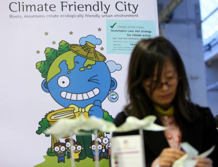 A woman makes paper windmills in front of an environmentalist poster at the Bella center of Copenhagen, capital of Denmark, December 14, 2009, during the UN Climate Change Conference.