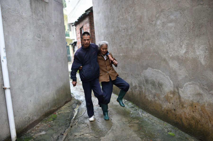 Huang Huiying helps her mentally-retarded son walk in the village. Huang's two sons also suffer from muscular atrophy which makes them unable to control their bodies' balance and even unable to walk. [Photo/Sina]