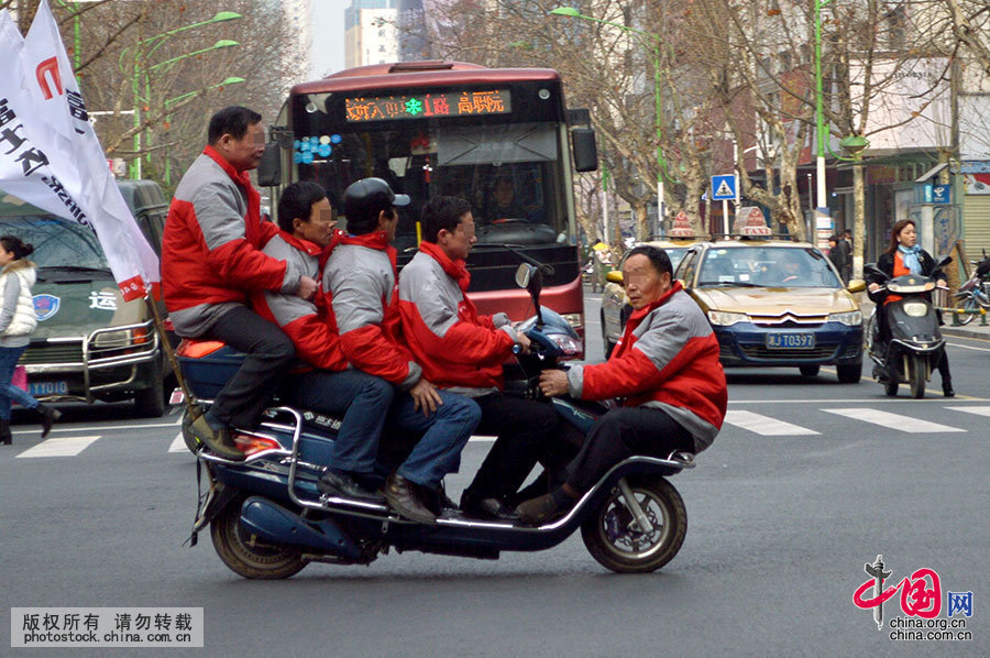  2014年3月16日上午，湖南常德城区青年路与人民路交叉路口，五条汉子坐在一电动车上宣传产品，上演马路“杂技”，路人呼叫“危险”。附近路段执勤交警为其拍照后进行了查纠。中国网图片库 陈自德 摄