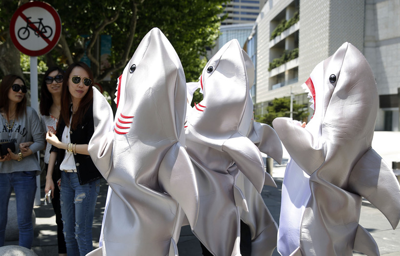Young persons, dressed as sharks, call for people to stop eating shark fins on a street in Shanghai on May 23, 2014. The non-governmental organization WildAid China launched the 'I'm FINished with FINS' campaign in Shanghai on Friday in efforts to call for people to stop eating shark fins and protect sharks. [Photo: China News Service / Tang Yanjun