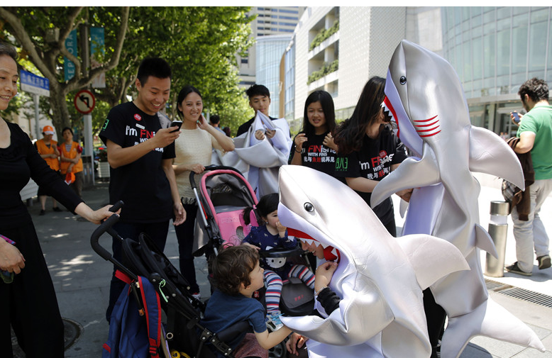 Young persons, dressed as sharks, call for people to stop eating shark fins on a street in Shanghai on May 23, 2014. The non-governmental organization WildAid China launched the 'I'm FINished with FINS' campaign in Shanghai on Friday in efforts to raise awareness of shark finning and help residents pledge not to eat shark fins. [Photo: China News Service / Tang Yanjun]