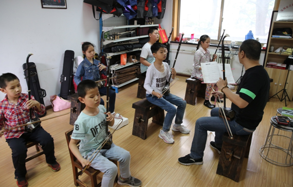 Li Chaoyi (R), founder of a non-profit instrumental training organization for disabled children, teaches blind children Erhu, a two-stringed bowed musical instrument, in Zhengzhou, capital of Henan Province, May 20, 2016. The organization founded by Li Chaoyi in 2014 has over ten volunteers by now, who have been teaching more than 50 blind children on music instruments. [file photo]