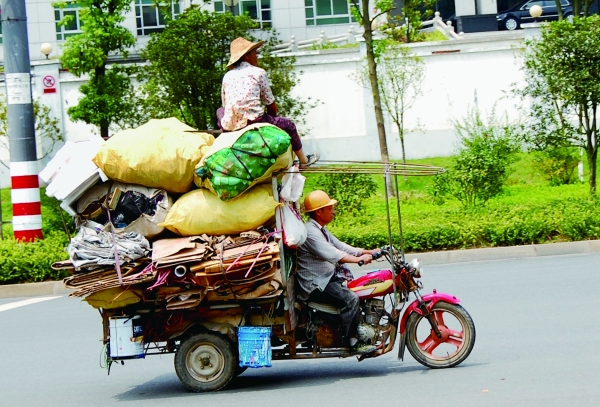 一辆满载著回收货物的三轮摩托车在路上疾驶