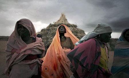 在沙尘暴来临之际，几名苏丹难民营的妇女站在泥草堆砌的房屋前。