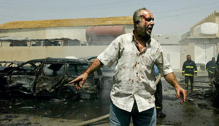 2006年6月17日，一名受伤的伊拉克男子指着在爆炸中被摧毁的汽车。