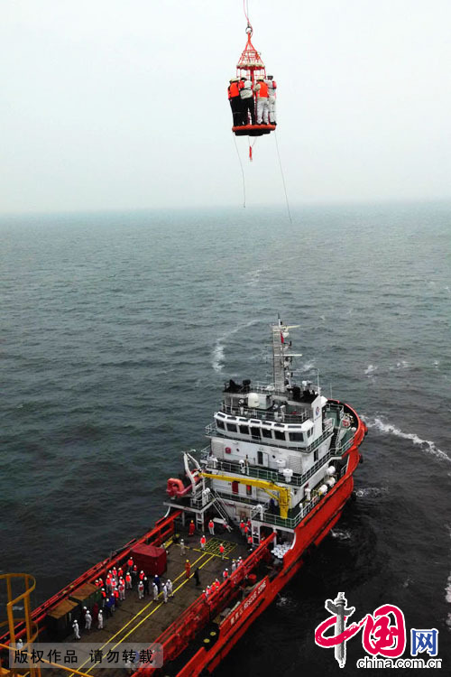 2014年10月1日，海洋石油（青島）工程有限公司的工人從120米高的海上石油平臺上下降到工作船上。中國網圖片庫 俞方平攝