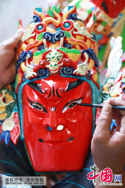  杨正洪在给雕刻好的面具上彩，一个面具要通过截林、剖半、出坯、白面、上彩等工序雕刻而成。中国网图片库 卢维摄