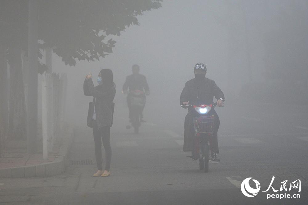 10月11日，市民戴着口罩在大雾行进，并沿途拍摄“没”景。（人民网记者翁奇羽 摄）