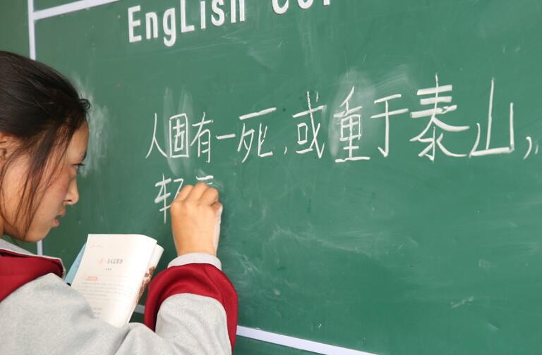 A second-year student in the Second Lhasa-Nagchu High School writes down a sentence from her Chinese textbook on the board. [Photo / China.org.cn]