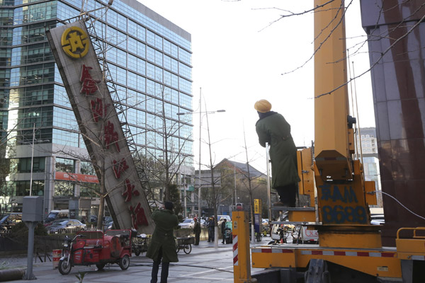 Workers remove a giant sign of a hotel in downtown Beijing last month that is deemed to have violated relevant regulations. [Photo/China Daily