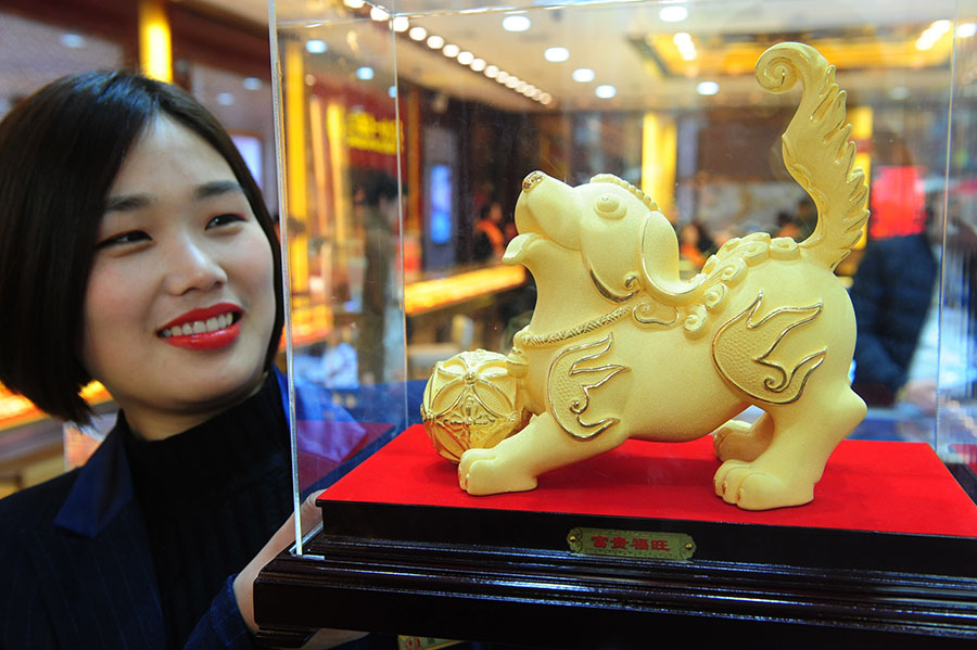 An employee of a jewelry shop in Fuyang, Anhui province, displays a dog statue made of gold. [Photo/China Daily]