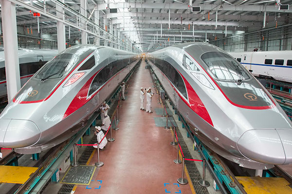 Workers check Fuxing bullet trains in the assembly workshop of CRRC Qingdao Sifang Co in Qingdao, Shandong province, in June. [Photo/Xinhua]